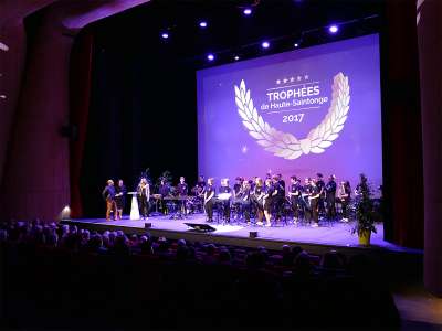 © Le Centre des Congrès de Haute-Saintonge et son architecture singulière primée L'entrée du Centre des Congrès de Haute-Saintonge lors d'un spectacle en nocturne Cérémonie des Trophées de Haute-Saintonge dans l'Auditorium Cérémonie des Journées Régionales de la Construction Bois dans l'Auditorium Cérémonie des Trophées de Haute-Saintonge dans l'Auditorium Cérémonie des 10 ans de la Maison de l'Emploi de Haute-Saintonge dans l'Auditorium Cérémonie des Journées Régionales de la Construction Bois dans l'Auditorium Concert à l'Auditorium à l'acoustique remarquable grâce au plafond en bois ondulé Concert à l'Auditorium à l'acoustique remarquable grâce au plafond en bois ondulé Concert à l'Auditorium à l'acoustique remarquable grâce au plafond en bois ondulé La cabine de traduction de l'Auditorium Le Studio TV du Centre des Congrès de Haute-Saintonge Concert à l'Auditorium à l'acoustique remarquable grâce au plafond en bois ondulé L'Agora en configuration gradins sortis L'Agora en configuration gradins sortis L'Agora en configuration gradins sortis Un concert dans l'Agora, configuration gradins sortis et parterre de danse Un concert dans l'Agora, configuration gradins sortis et parterre de danse Concert dans l'Agora Soirée cabaret dans l'Agora, gradins rétractés, tables rondes sur le parterre Thé dansant dans l'Agora, gradins rétractés, tables rondes et parterre de danse Repas dans l'Agora, gradins rétractés, tables rectangulaires Repas dans l'Agora, gradins rétractés, tables rectangulaires Mise en place pour un repas dans l'Agora avec tables rectangulaires Exposition dans le Hall d'entrée de 600m² Le Hall d'entrée de 600m² et son bar Exposition dans le Hall d'entrée de 600m² Le Hall d'entrée de 600m² Le Hall d'entrée de 600m² du haut de l'escalier monumental Le Hall d'entrée de 600m² du haut de l'escalier monumental un soir de concert Vue imprenable sur la vallée de la Seugne et la campagne haute-saintongeaise Le Hall d'entrée de 600m² en configuration repas buffet Le Hall d'entrée de 600m² en configuration repas-buffet lors d'une réunion de travail Le Hall d'entrée de 600m² en configuration repas-buffet lors d'une réunion de travail Un congressiste dans le Hall d'entrée de 600m² en configuration repas-buffet Petit déjeuner d'accueil dans le Hall d'entrée de 600m² lors d'un congrès Le bar du Hall d'entrée de 600m² Le bar du Hall d'entrée de 600m² Réunion de travail dans une des salles de séminaires Réunion de travail dans une des salles de séminaires Réunion de travail dans une des salles de séminaires Une des six salles de séminaires Une des six salles de séminaires Une des six salles de séminaires Une salle de séminaire transformée en salle d'exposition Une salle de séminaire transformée en salle d'exposition Une des sept loges Une des sept loges Une des sept loges